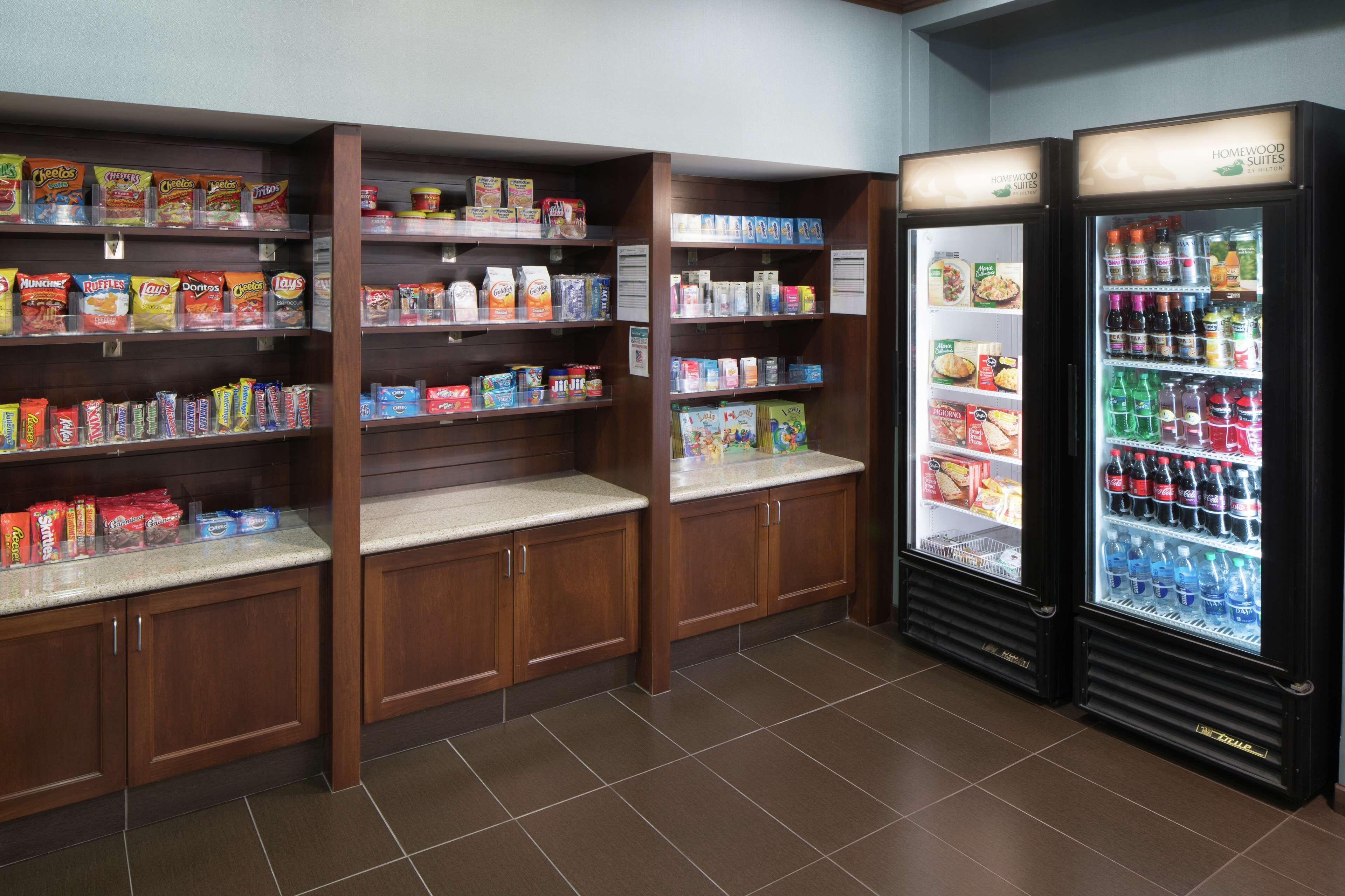 A self-service snack and beverage area with shelves stocked with various snacks and drinks, and two refrigerated beverage dispensers.