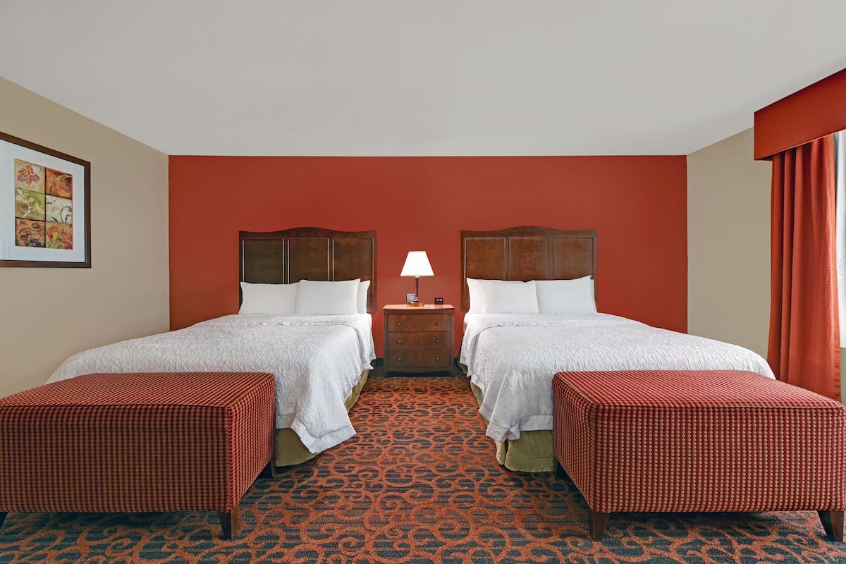 A hotel room with two beds, a nightstand with a lamp, and a patterned carpet.