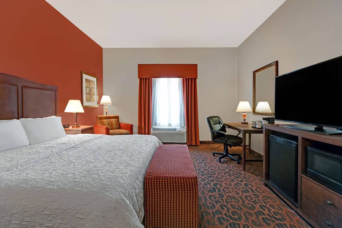 A hotel room with a large bed, a desk, a television, and a window with curtains.