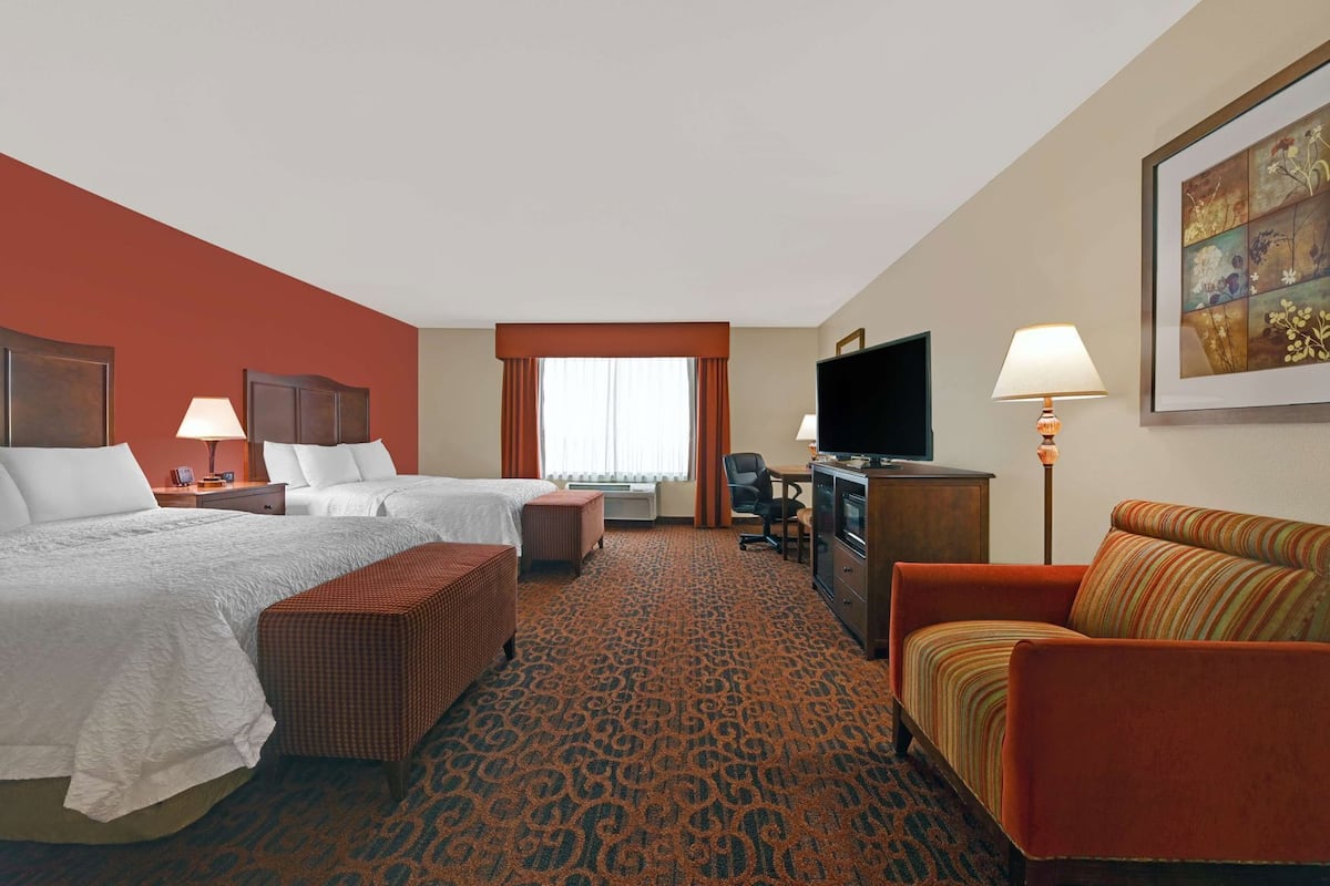 A hotel room with two beds, a sofa, a TV, a desk, and a chair.