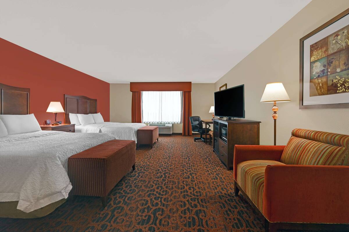 A hotel room with two beds, a desk, a television, and a sofa.