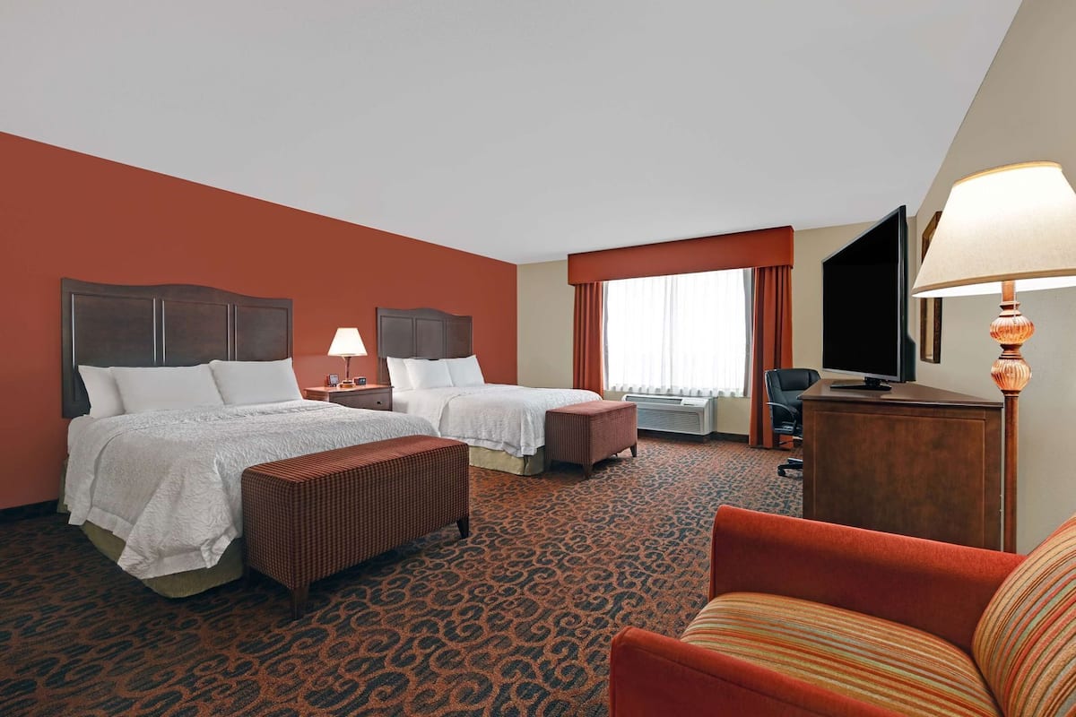 A hotel room with two beds, a TV, a desk, a chair, and a lamp.