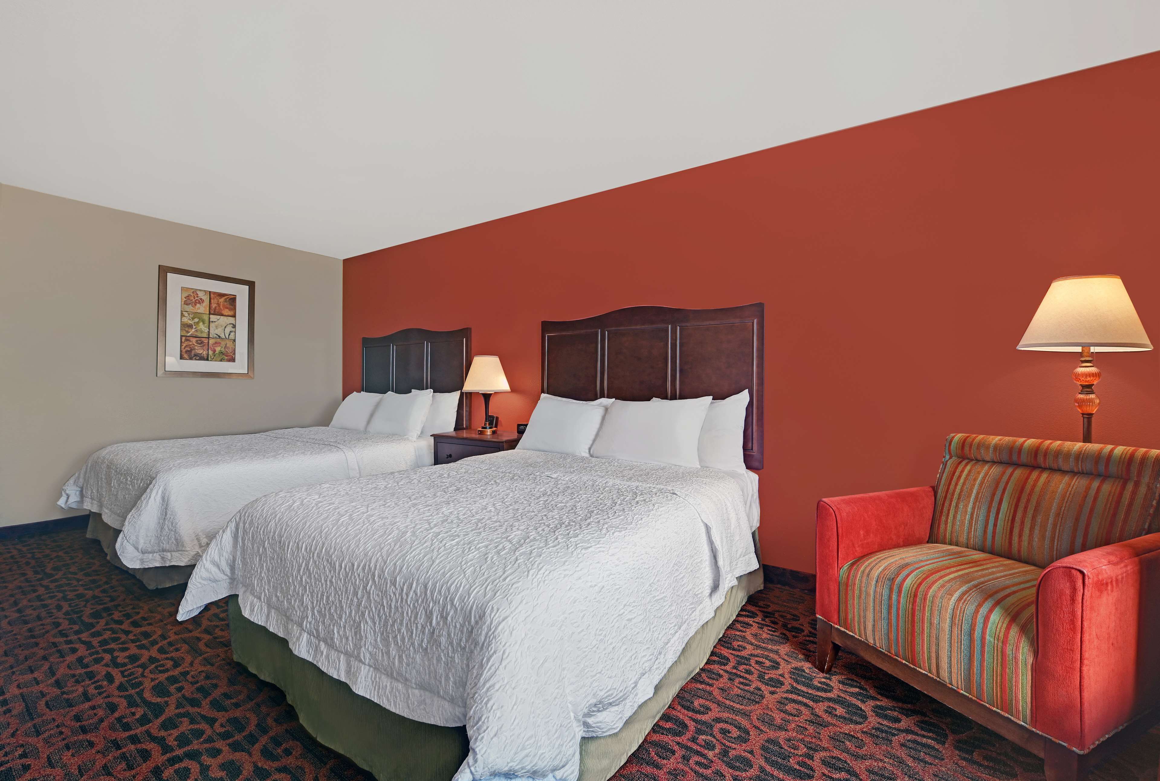 A hotel room with two beds, a red armchair, and a patterned carpet.
