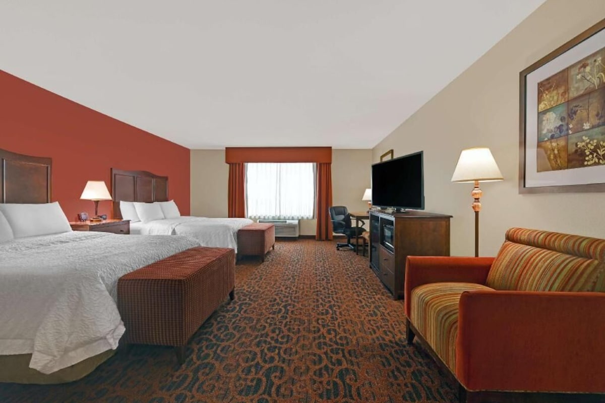 Quarto de hotel com duas camas, um sofá, uma escrivaninha, uma televisão e um quadro na parede.