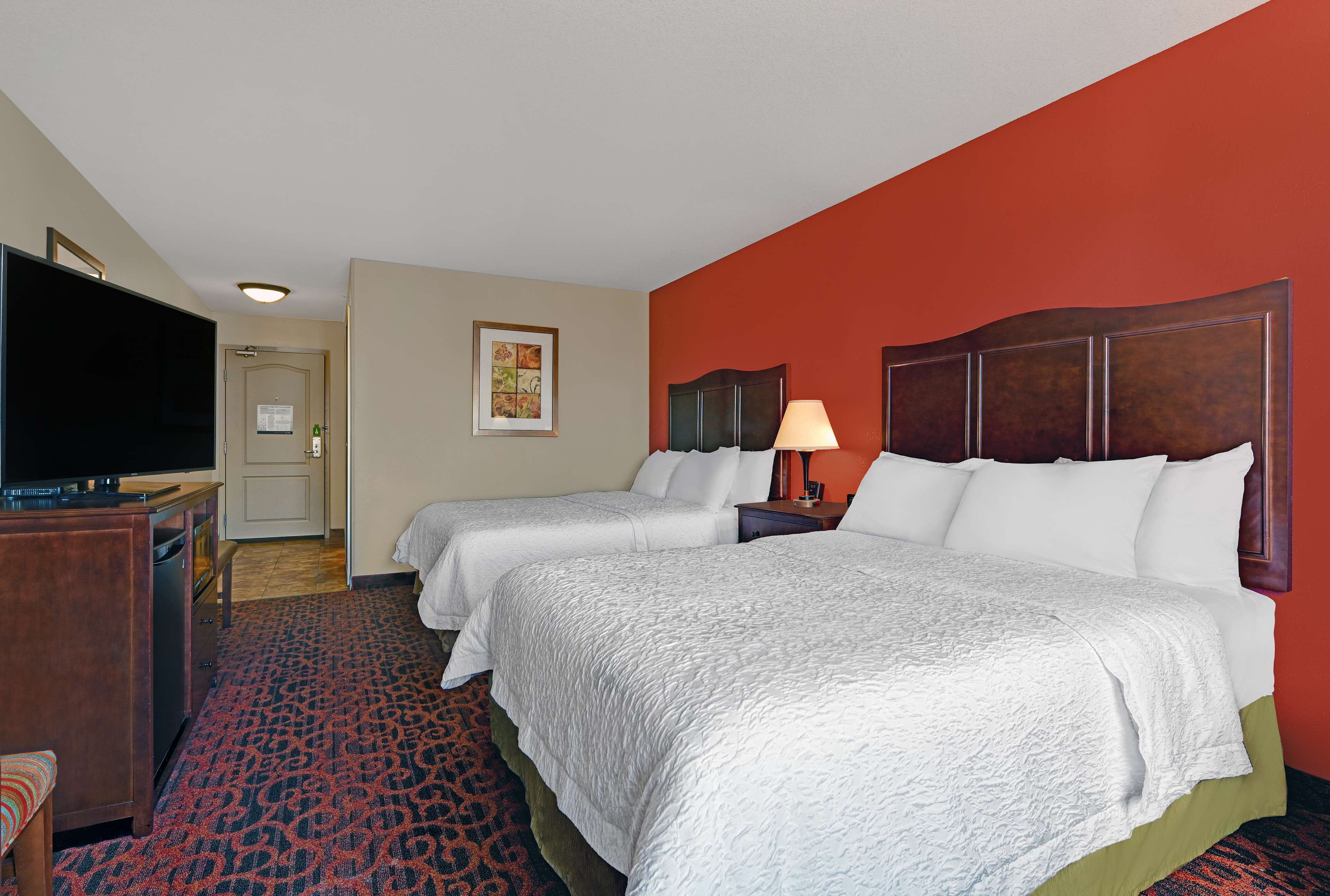 Une chambre d’hôtel avec deux lits, une télévision, un bureau et un mur d’accent de couleur rouge.
