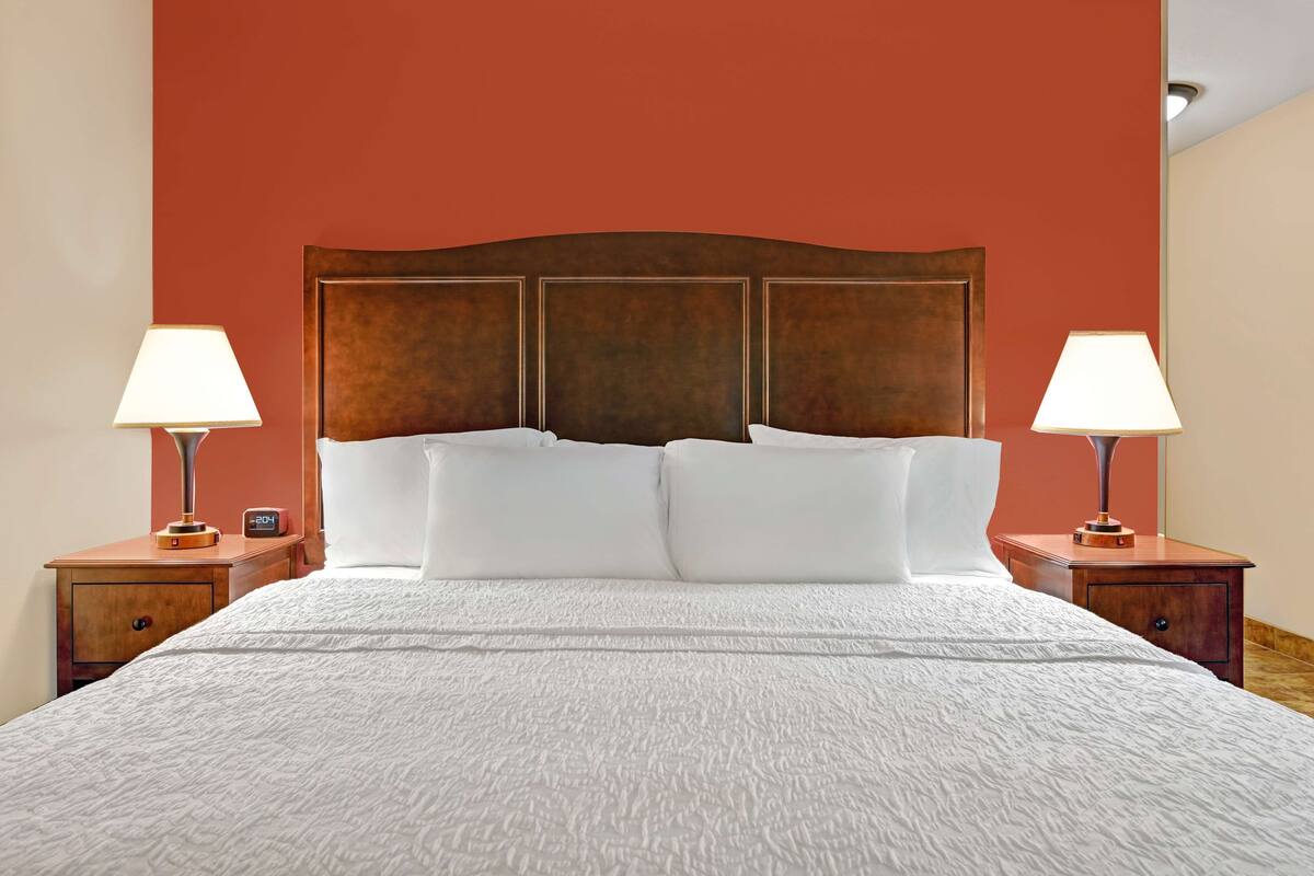A neatly made bed with white linens and a wooden headboard, flanked by two bedside tables with lamps and clocks.