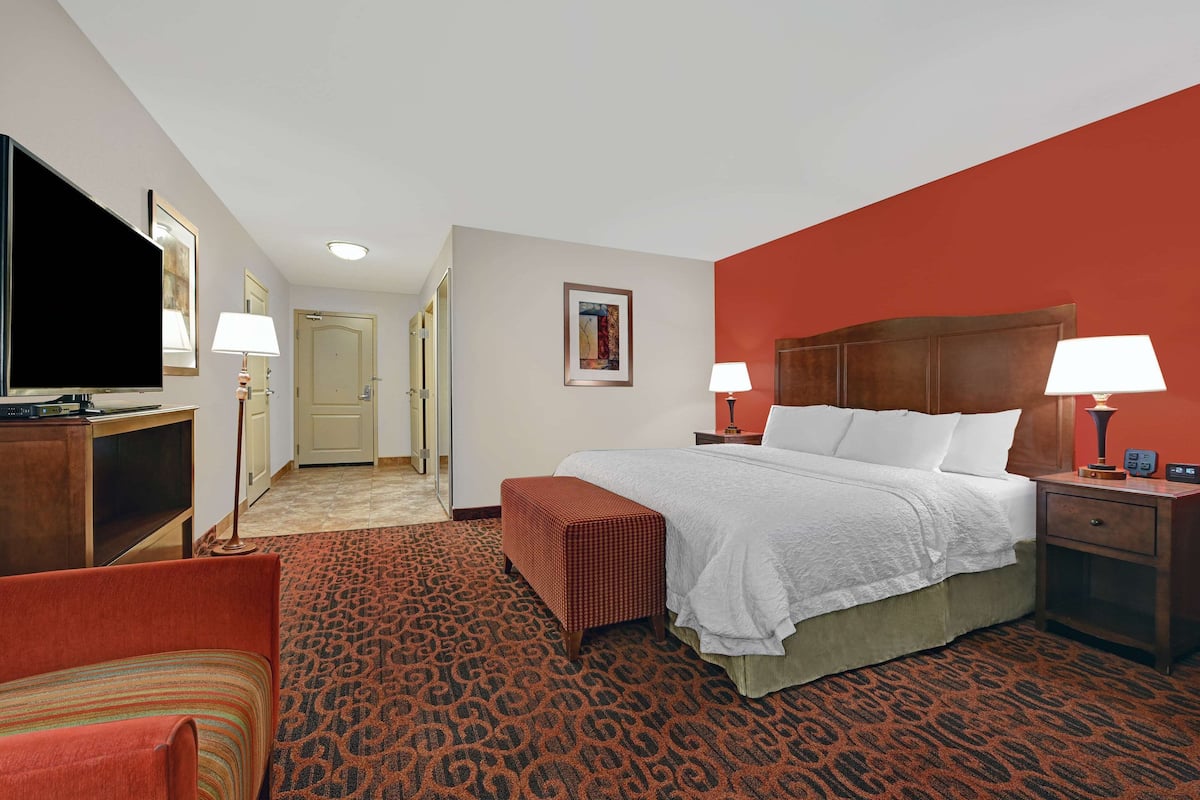 A hotel room with a bed, two bedside tables with lamps, a television, a red armchair, and a patterned carpet.