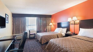 A hotel room with two beds, a desk, a chair, a TV, and a window with curtains. - Rodeway Inn Meadowlands (Secaucus)