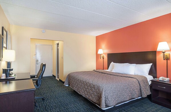 A hotel room with a bed, desk, chair, and two bedside lamps. - Rodeway Inn Meadowlands (Secaucus)