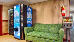 A lobby with vending machines, a green patterned sofa, and a fire extinguisher on the wall. - Rodeway Inn Meadowlands (Secaucus)