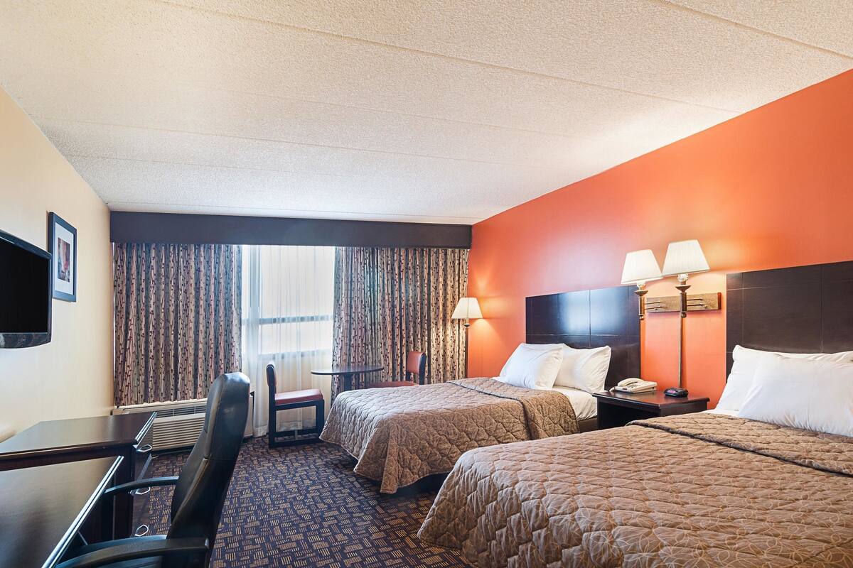 Une chambre d’hôtel avec deux lits, un bureau, une chaise, une télévision et une fenêtre avec des rideaux.