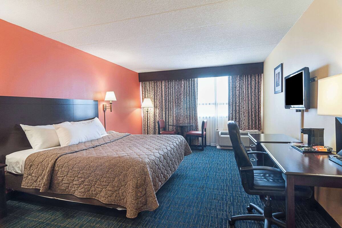 Une chambre d’hôtel avec un lit, un bureau, une chaise, une télévision et une fenêtre avec des rideaux.
