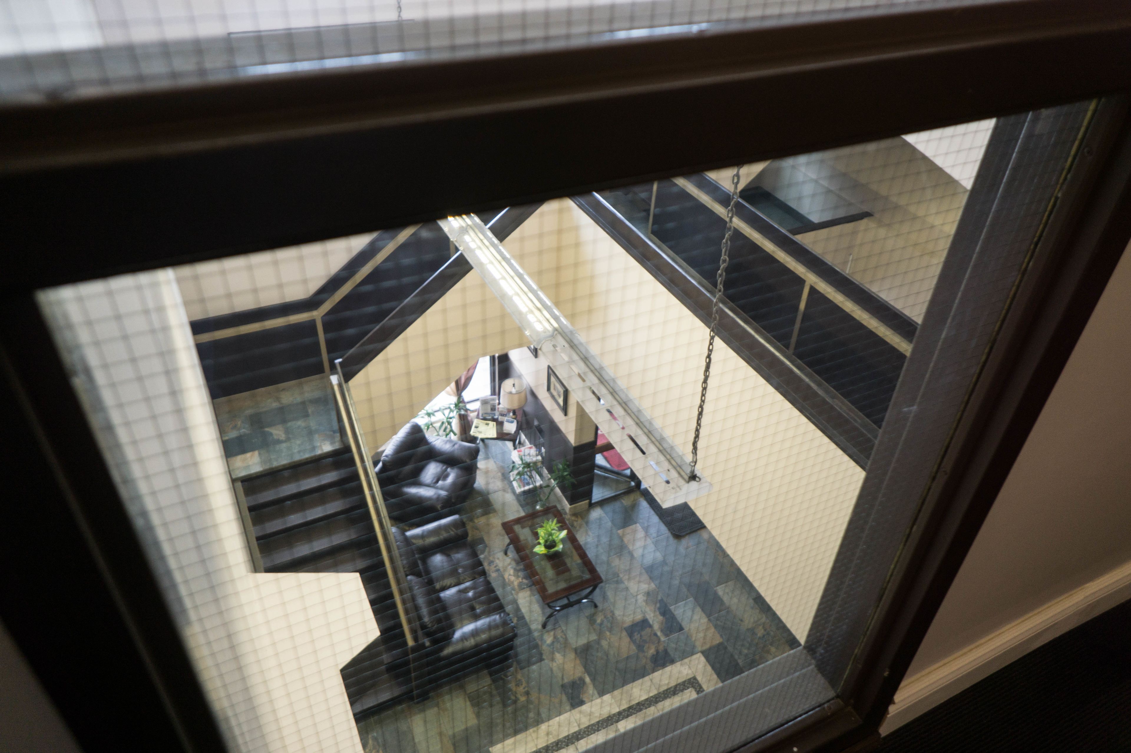 Vista interior de un vestíbulo de hotel con un sofá de cuero negro, una pequeña mesa con una planta y una escalera al fondo.