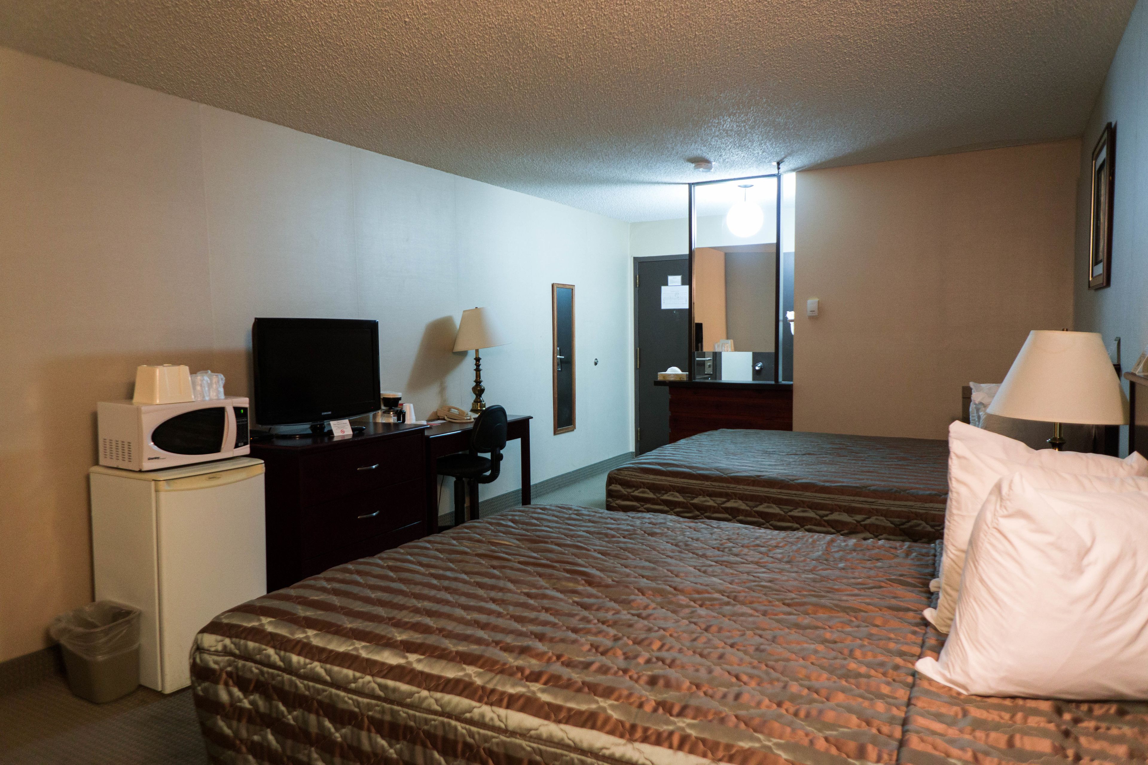 A hotel room with two beds, a desk with a computer, a microwave, and a television.