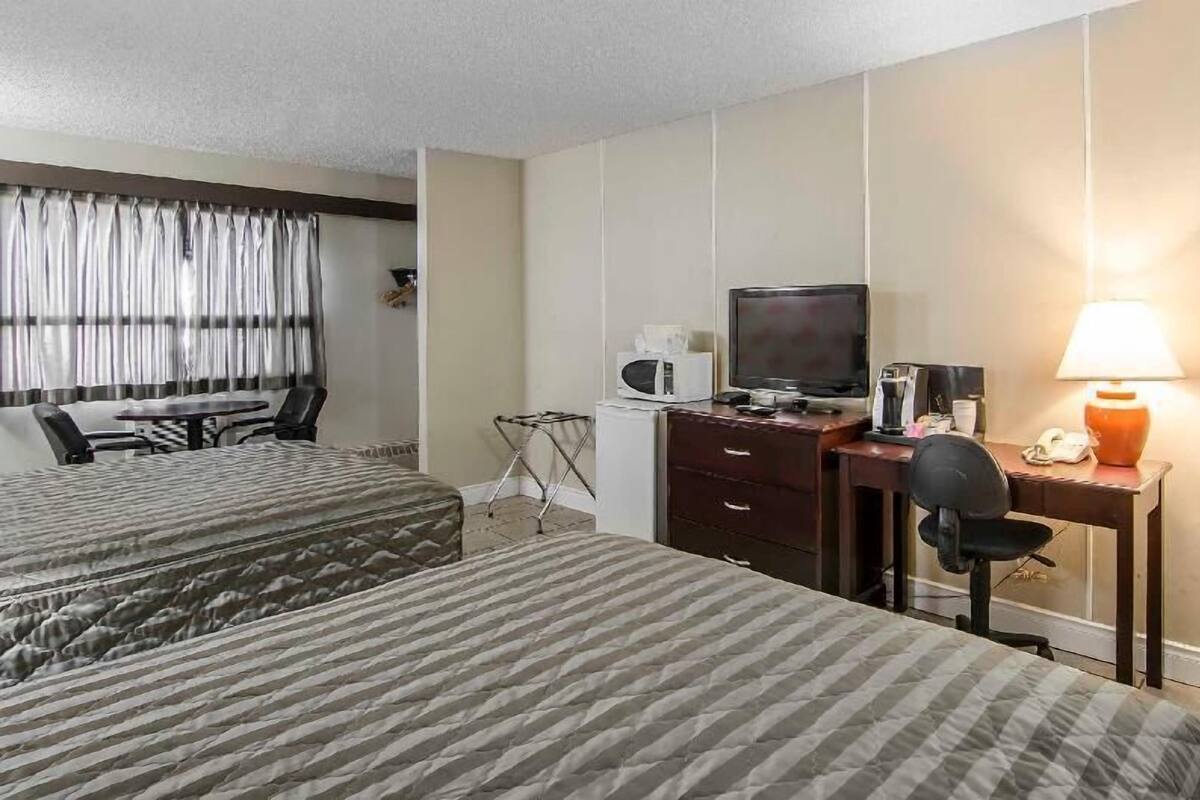 Une chambre d’hôtel avec deux lits, un bureau avec un ordinateur, une télévision, une lampe et un four à micro-ondes.