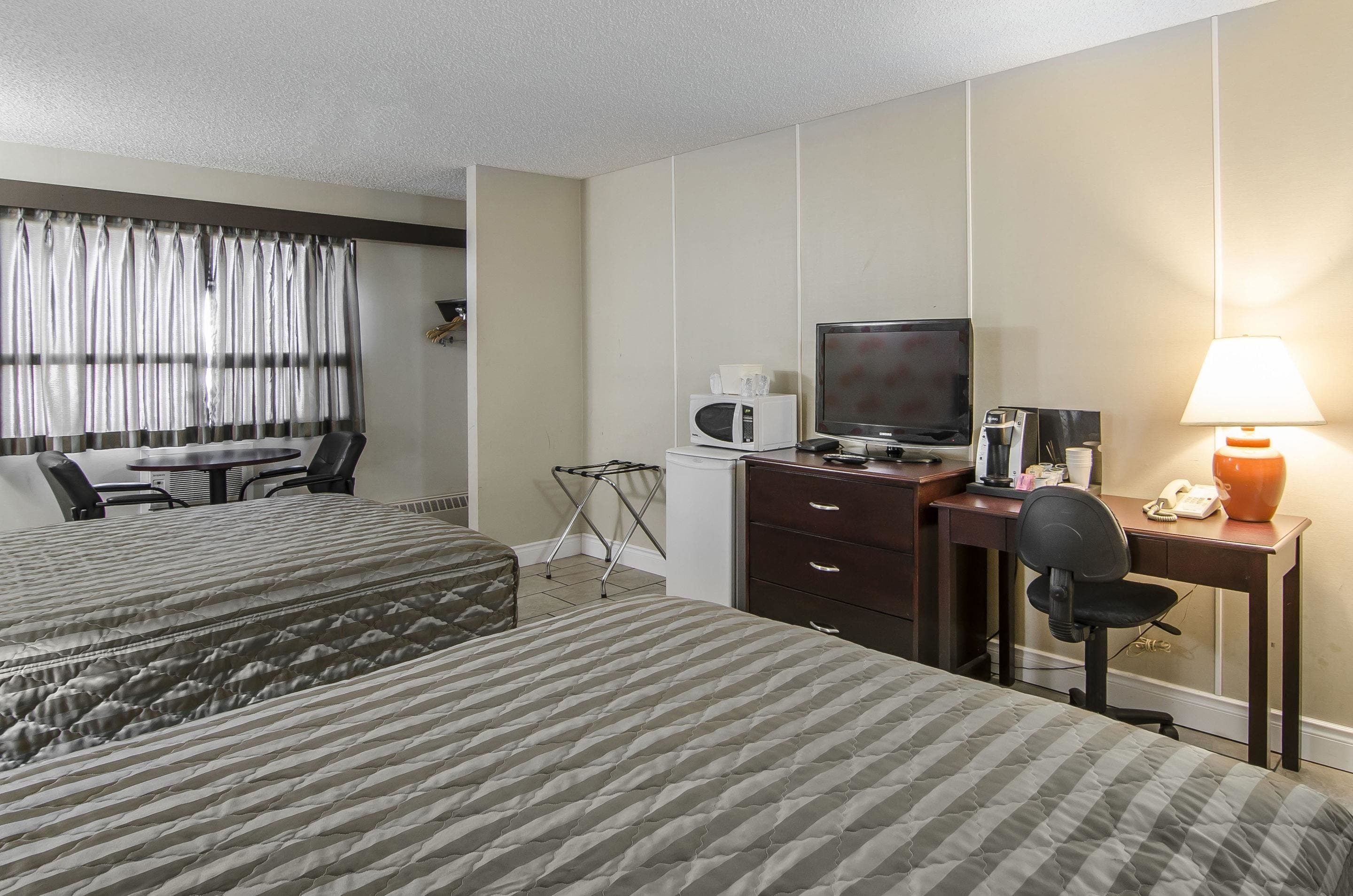 Una habitación de hotel con dos camas, un escritorio con computadora, un televisor y una lámpara.