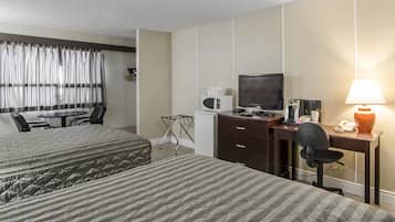 Una habitación de hotel con dos camas, un escritorio con computadora, un televisor y una lámpara.