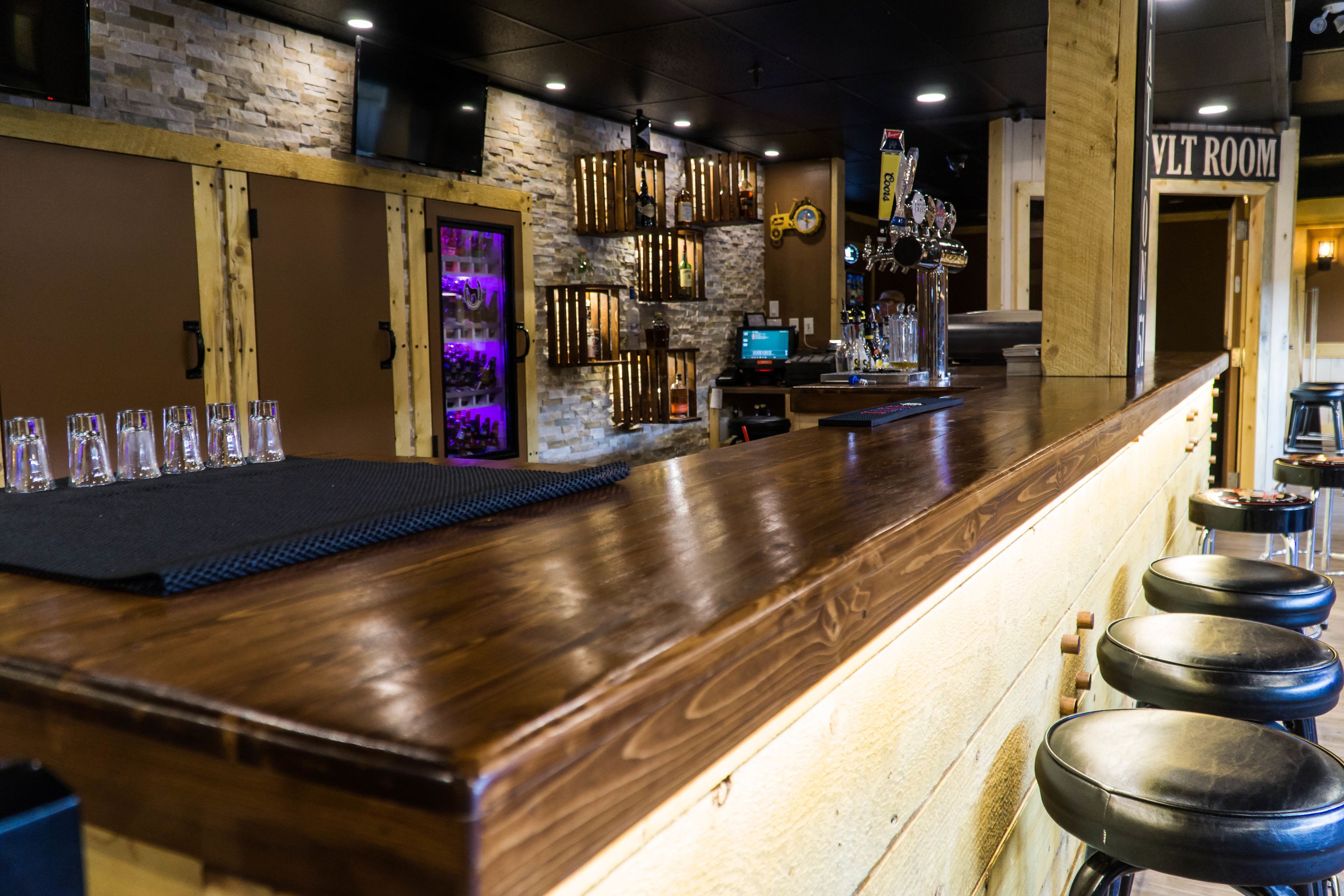 A bar area with a wooden counter, stools, and a TV screen.