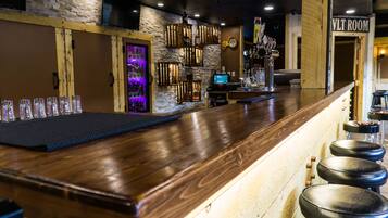 A bar area with a wooden counter, stools, and a TV screen.