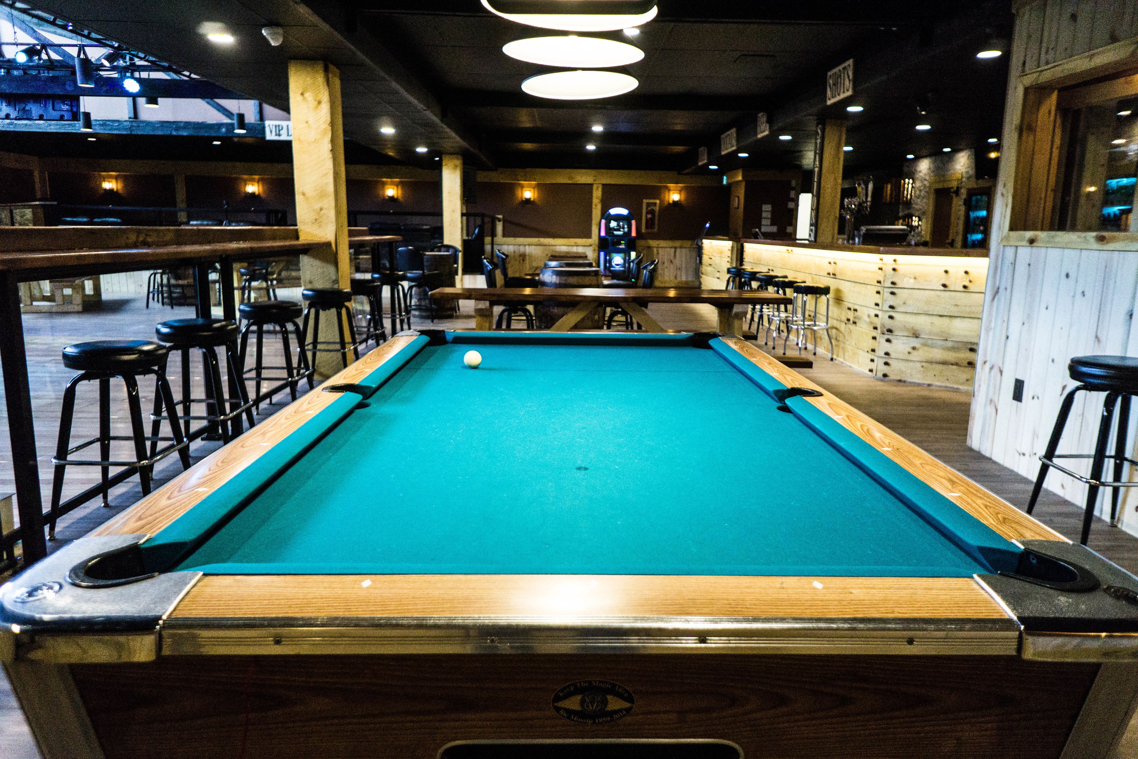 A pool table in a bar area with stools around it.