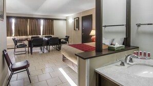 Habitación de hotel con cama, escritorio, silla y baño con lavamanos y espejo.