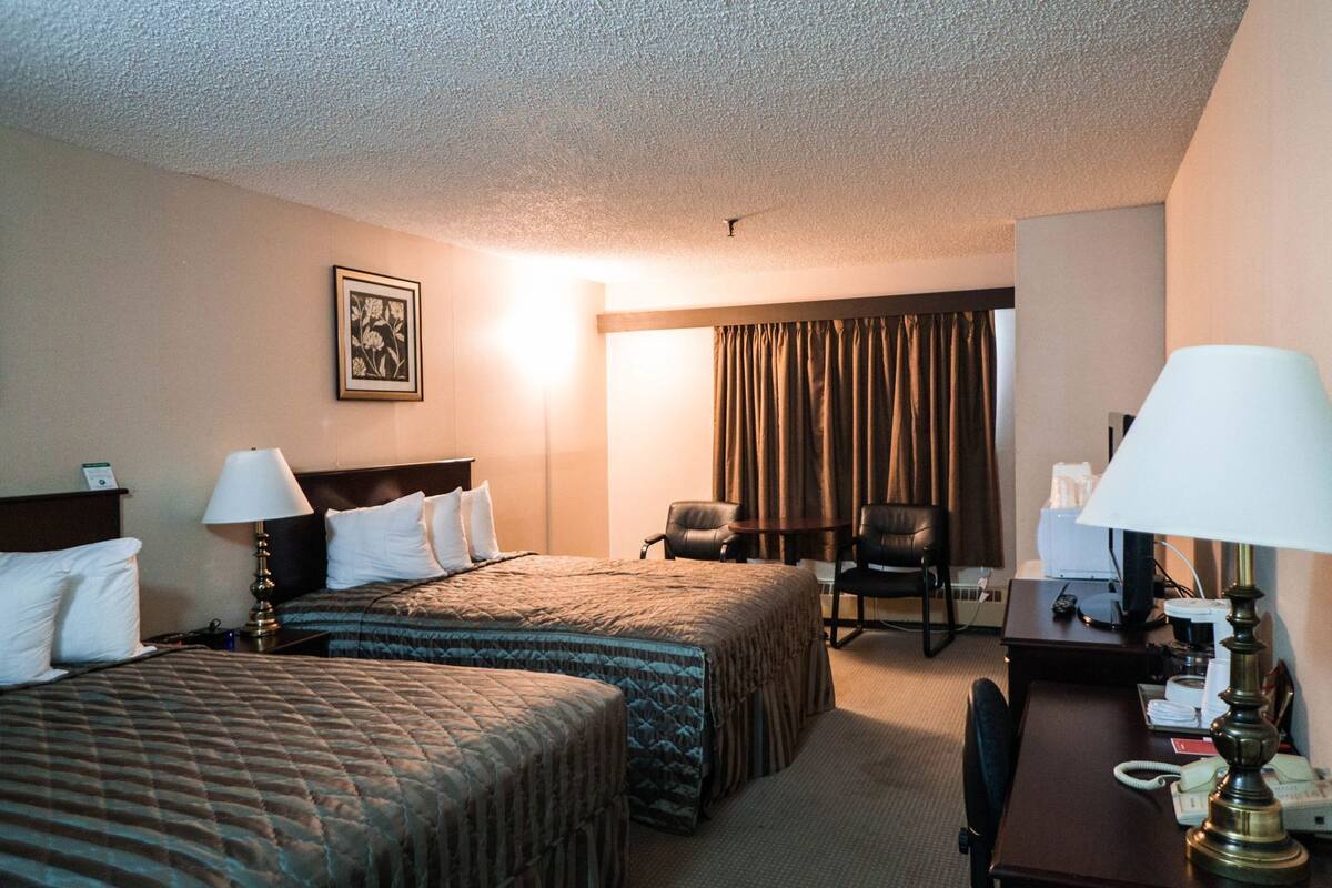 Une chambre d’hôtel avec deux lits, un bureau, une chaise et une lampe.