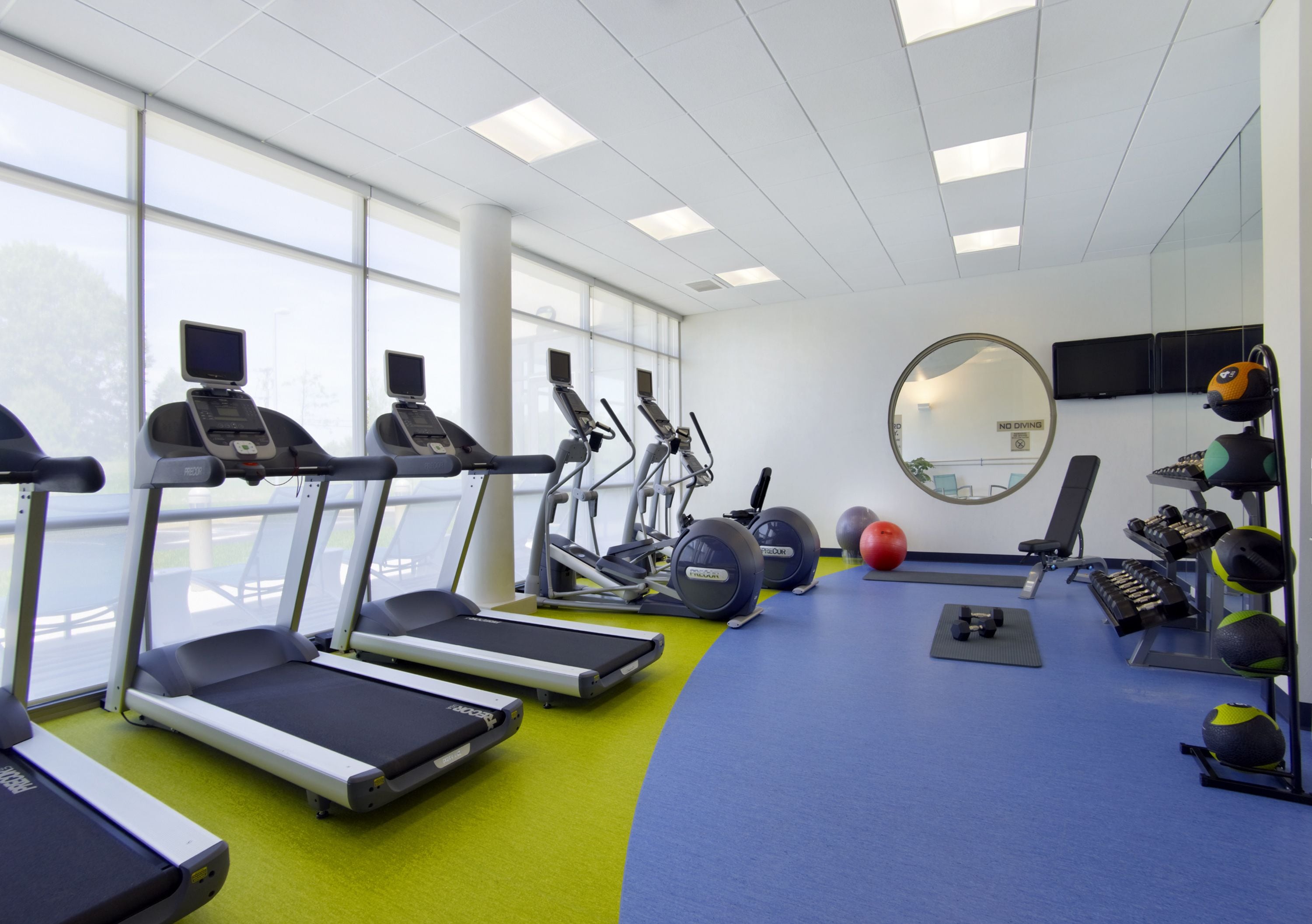 A gym with treadmills, elliptical machines, and exercise balls.