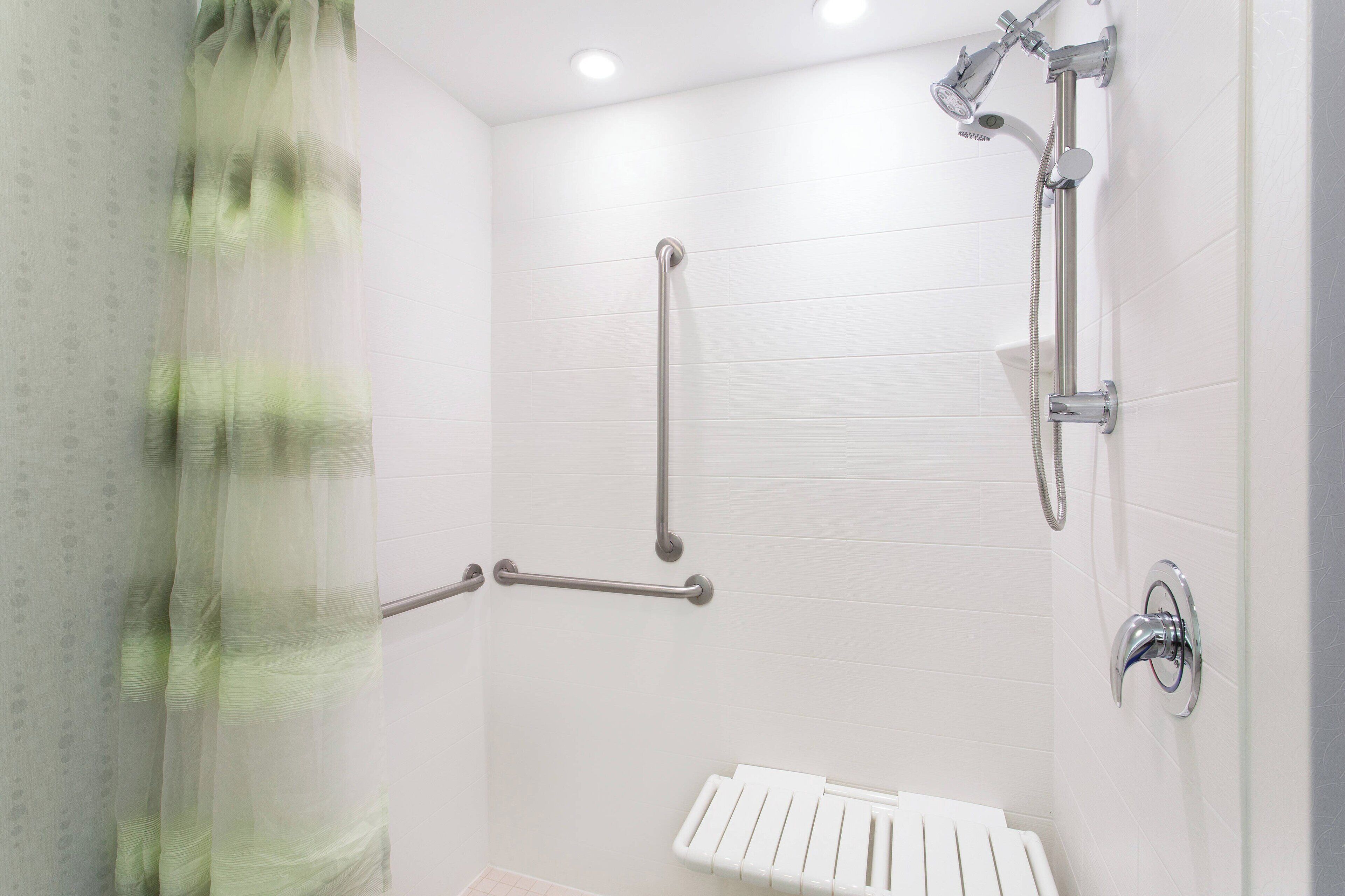 Ducha con cabezal de ducha de mano, barras de apoyo y un perchero blanco.