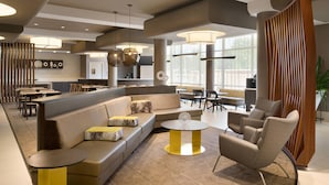 A modern hotel lobby with a seating area, a bar, and a dining space.
