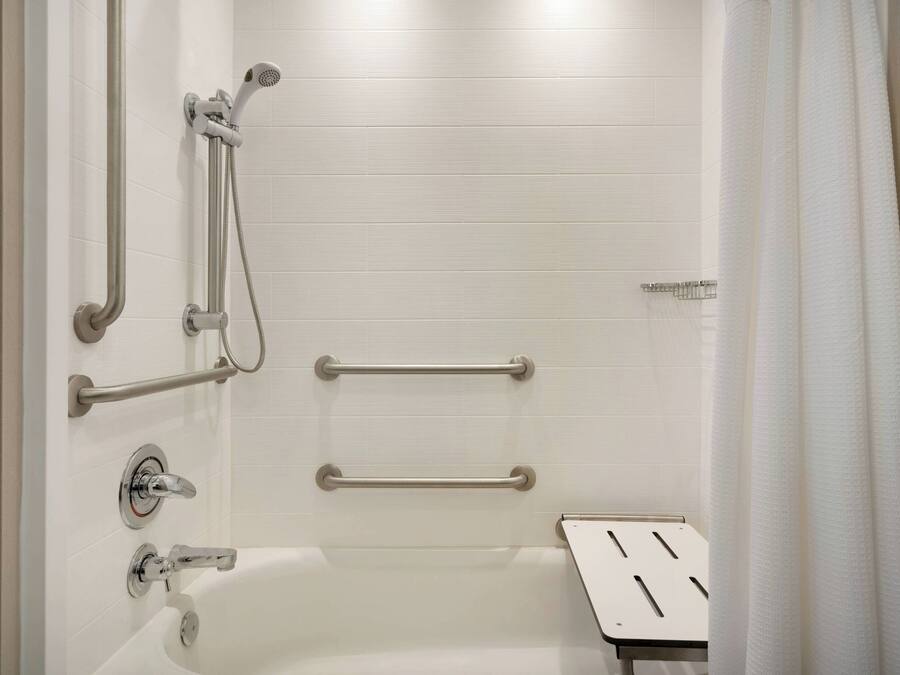 A modern bathroom with a white bathtub, grab bars, and a showerhead.