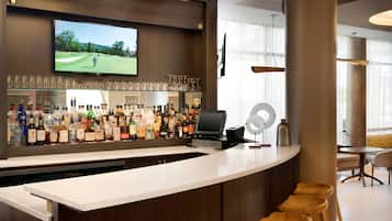 A bar area with a television displaying a golf game, a variety of liquor bottles, and a cash register.