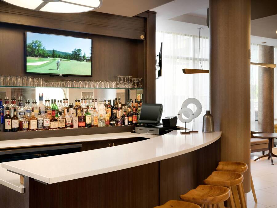 A bar area with a television displaying a golf game, a variety of liquor bottles, and a cash register.