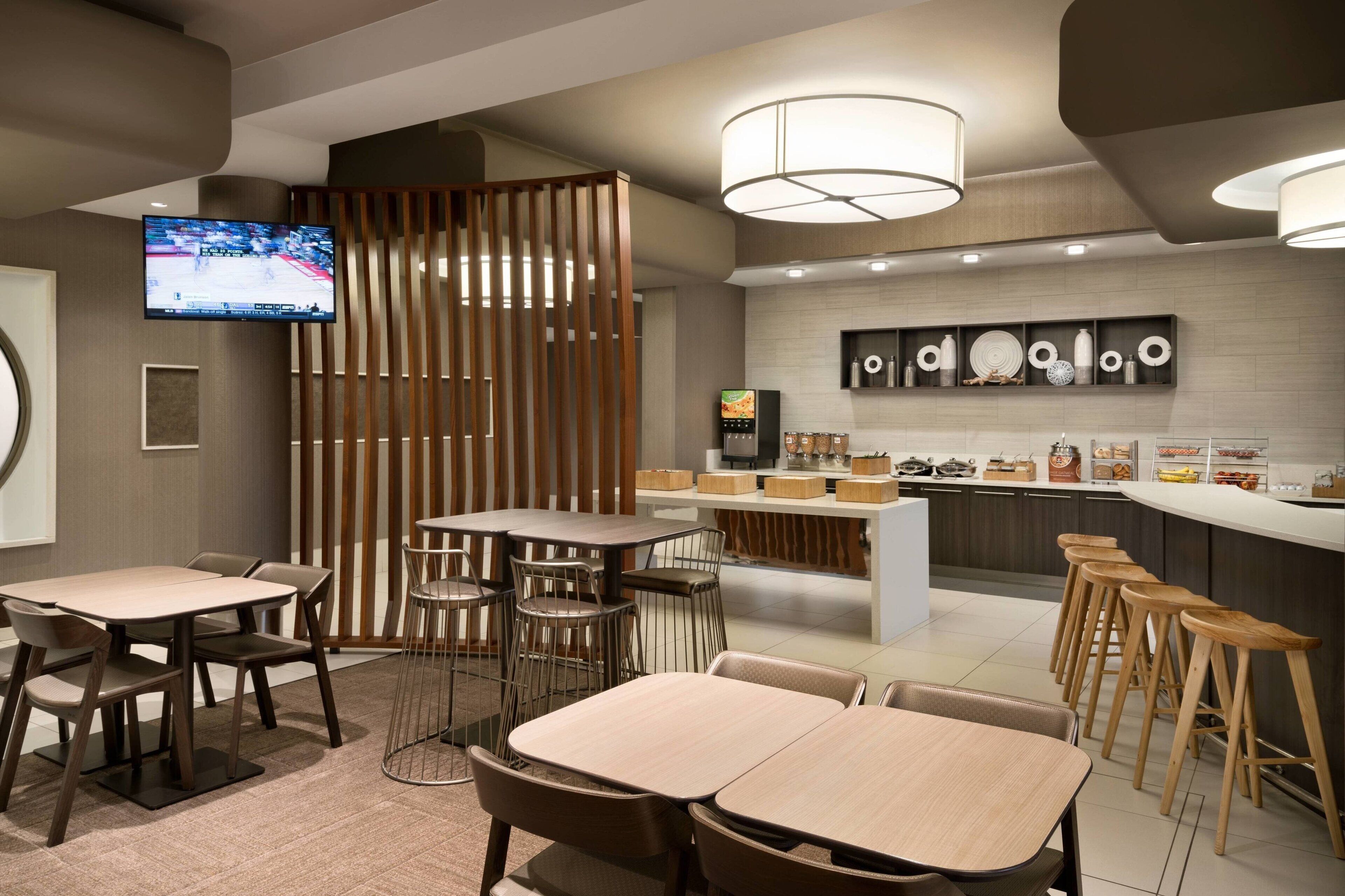 Un restaurante moderno con mesas, taburetes, una zona de cocina y un televisor que muestra deportes.