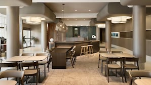 A modern restaurant with a central bar area, multiple seating options including tables and stools, and pendant lighting.