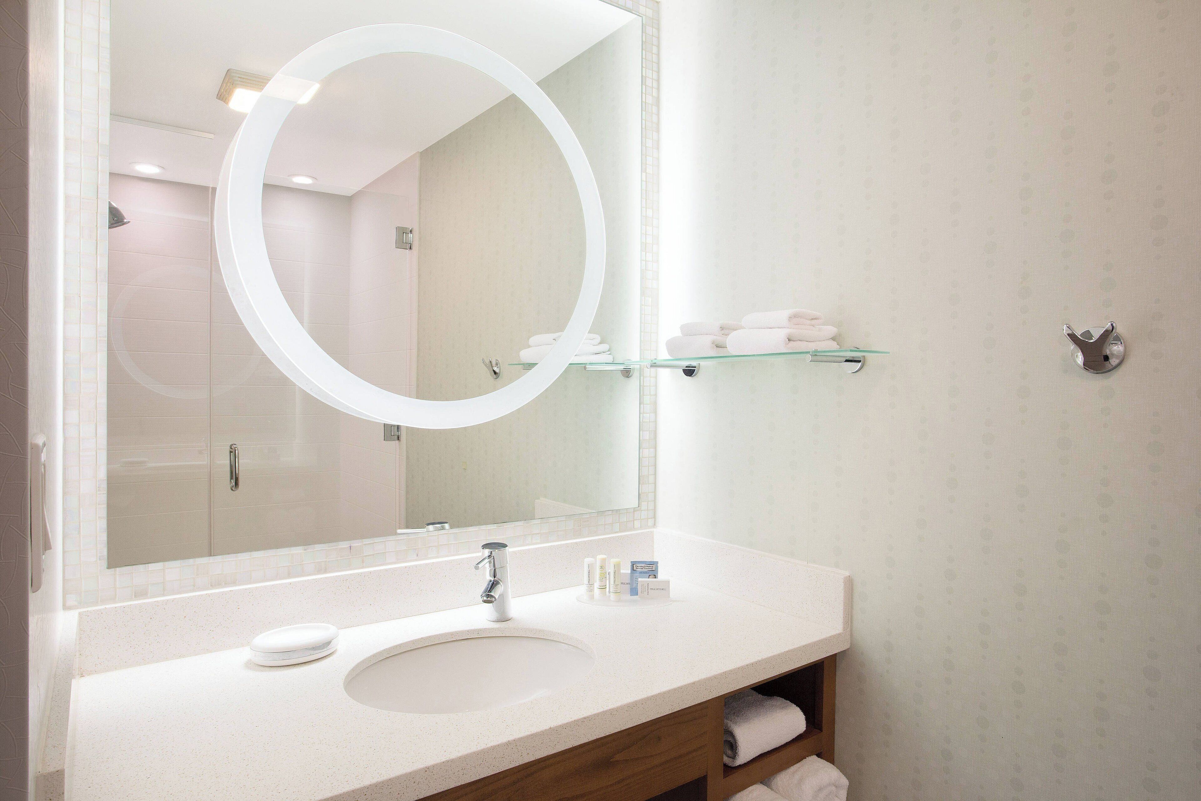 Une salle de bain avec un grand miroir, un lavabo et une étagère en verre où sont posées des serviettes.