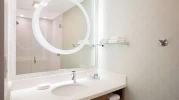 A bathroom with a large mirror, a sink, and a glass shelf with towels.