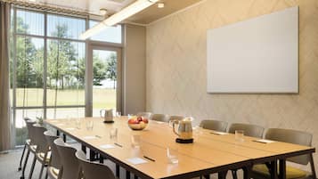A conference room with a long table, chairs, a projector screen, and a window with a view of trees.