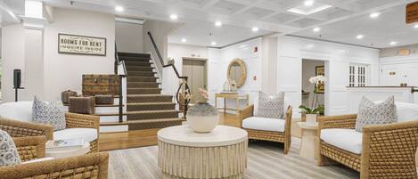 A hotel lobby with wicker furniture, a staircase, and a sign indicating rooms for rent.