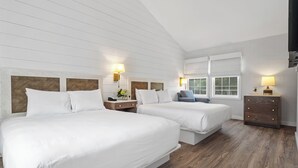 A hotel room with two beds, wooden floors, white walls, and a sloped ceiling.