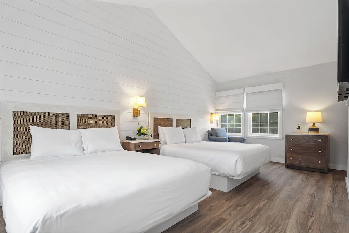 A hotel room with two beds, wooden floors, white walls, and a sloped ceiling.