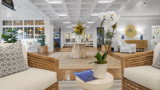 A spacious lobby with wicker furniture, a registration sign, a central table with a vase of flowers, and a book titled 'Nantucket'.