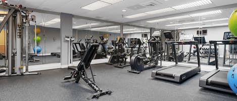 Ett gym med konditionsmaskiner, styrketräningsutrustning och speglar på väggarna.