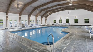 An indoor swimming pool with clear blue water, surrounded by lounge chairs and a tiled floor.