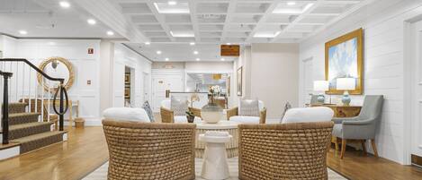 Um hall amplo com área de estar central, escada com guarda-corpo decorativo e uma grande obra de arte emoldurada na parede.