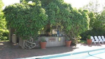 A pool area with a small structure surrounded by potted plants and white chairs.