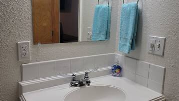 A bathroom with a white sink, a mirror, two towels hanging on towel bars, a soap dispenser, and a toilet paper holder.