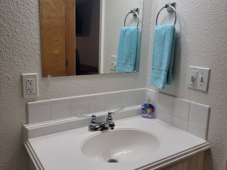 A bathroom with a white sink, a mirror, two towels hanging on towel bars, a soap dispenser, and a toilet paper holder.