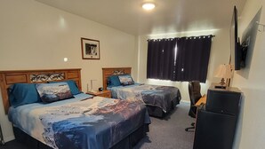 Habitación de hotel con dos camas, un escritorio, una silla, un televisor y un ventilador de techo.
