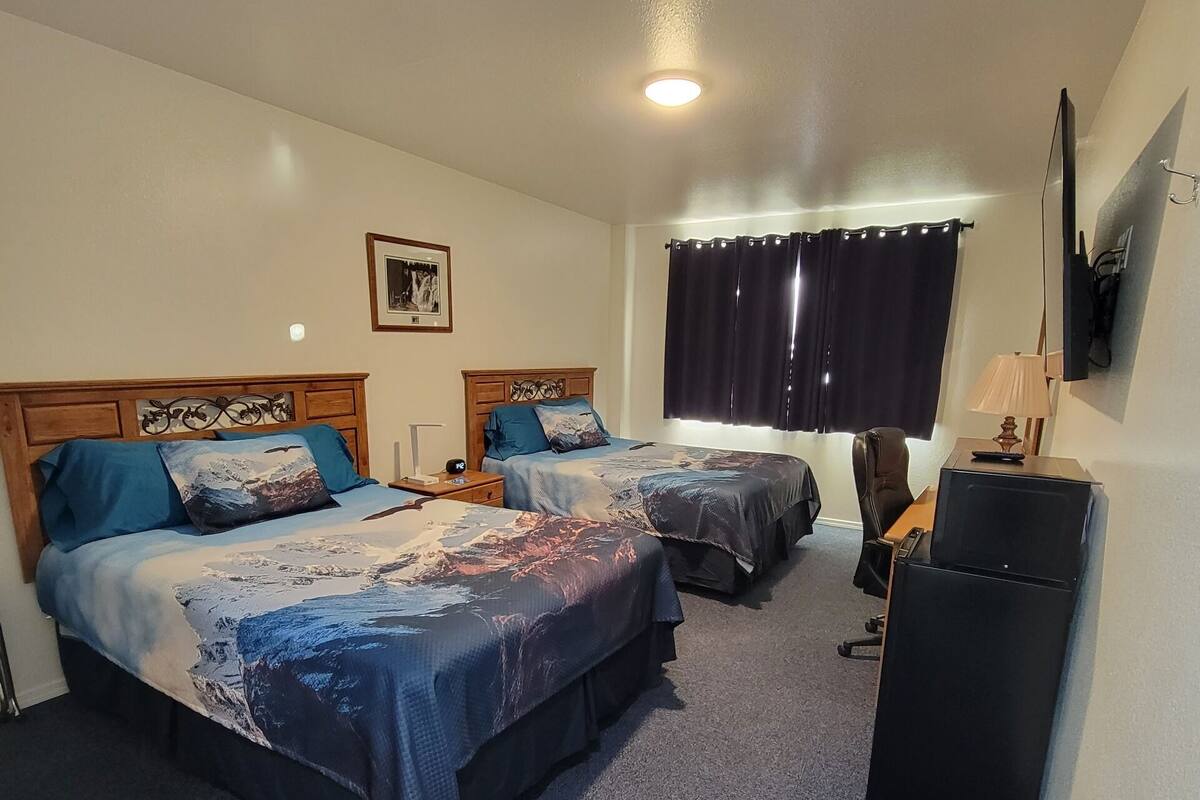 A hotel room with two beds, a desk, a chair, a TV, and a ceiling fan.