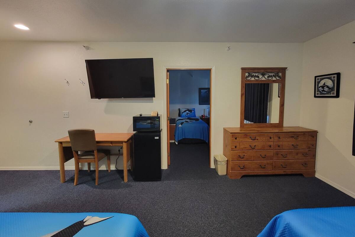 A hotel room with a desk, chair, dresser, TV, and two beds.